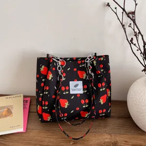 Detail shot of the black floral tote bag featuring strawberry print, chain straps and fabric label.