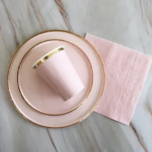Nahaufnahme von rosa Papptellern und Bechern mit Goldrand ordentlich arrangiert auf Marmor.