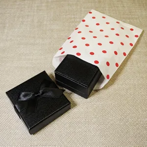 Cajas de regalo negras con lazo y bolsas de papel de lunares, ideales para empaquetar joyas.