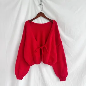 Primo piano di un cardigan in maglia rossa con chiusura a fiocco e trama testurizzata.