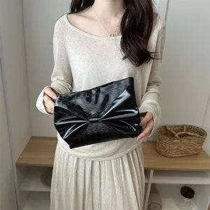 Detail view of black patent leather clutch bag with large bow, elegant evening fashion accessory.