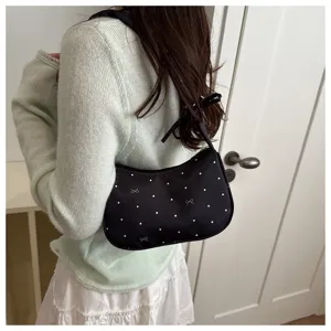 Detail shot of a chic black crescent shoulder bag with white polka dots and bow accents.