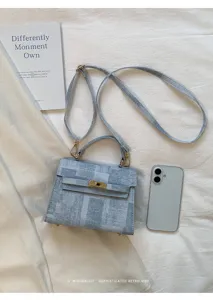 Sac porté épaule structuré en denim bleu avec fermoir tourniquet en métal et bandoulière.