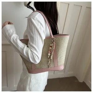 Detail view of women summer straw woven shoulder bag with pink leather trim and wooden bead charm.