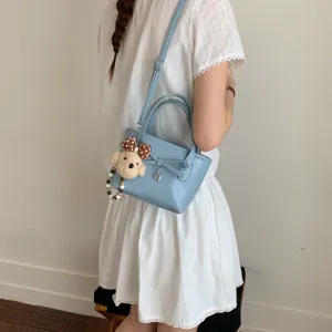 Borsa a mano azzurra da donna con grazioso fiocco e ciondolo orsetto a tracolla.