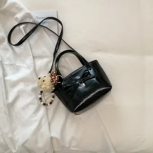 Elegante borsa secchiello in pelle verniciata nera con fiocco e grazioso orsetto.