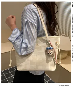 Detailansicht einer stilvollen karierten Schultertasche mit einem süßen Bären-Plüschanhänger.
