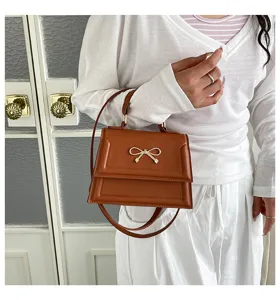 Détail élégant de sac à bandoulière en cuir marron avec accent de nœud doré raffiné.