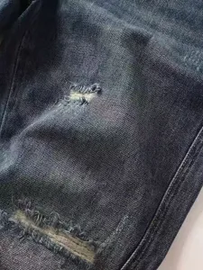 Vista dettagliata ravvicinata della trama in denim scuro slavato e strappi da uomo.