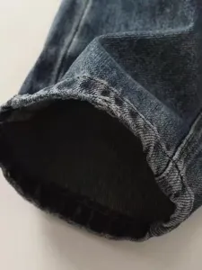 Primo piano del tessuto denim scuro, con dettagli sulla trama dell'orlo usurato e cuciture precise.