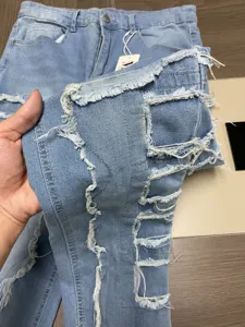 Jean en denim bleu clair vieilli avec bords effilochés, patches et coupe droite détaillée.