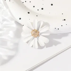 Close-up detail shot of white enamel daisy brooch featuring textured gold flower center and petals.