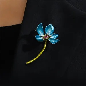 Close-up shot of a vintage blue enamel lotus brooch with pearl and crystal details on fabric.