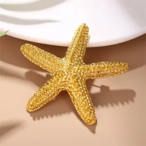 Close-up detail shot of a gold alloy starfish brooch, featuring textured surface and shiny finish.