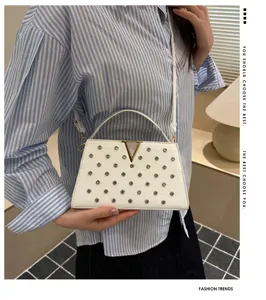 Vue détaillée du sac bandoulière blanc et élégant avec des clous et un logo V doré.