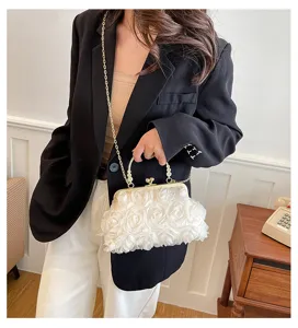 Dettaglio elegante di una pochette bianca in tessuto con rose 3D e catena d'oro.