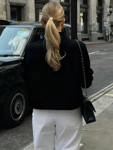 Detail view of stylish black blazer jacket paired with white trousers and classic chain bag.