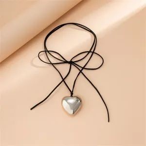 Gros plan détaillé d'un collier pendentif cœur argenté avec cordon en velours noir.