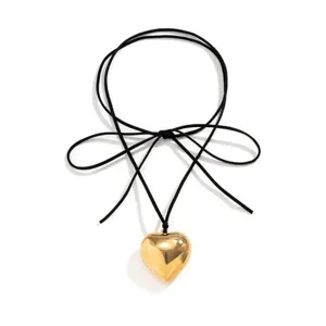 Gros plan detail du collier en cordon de velours noir avec un pendentif coeur dore.