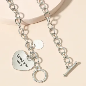 Close-up of retro silver tone heart pendant necklace featuring toggle clasp and engraved text.