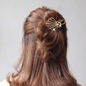 Detalle de la pinza de pelo en forma de concha dorada con elegante diseño metálico.