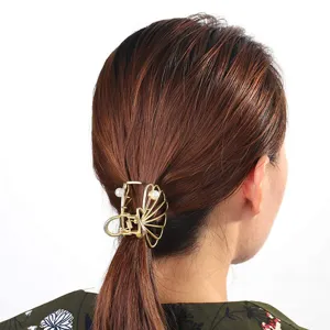Detalle de pinza de pelo de garra geométrica hueca de metal con perla, diseño dorado.