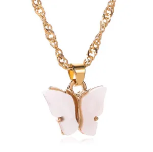 Goudkleurige metalen ketting met een delicaat wit acryl vlinderhanger detail in close-up view.