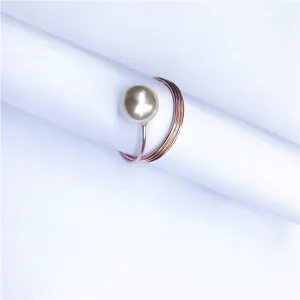 Dettaglio in primo piano di un elegante anello portatovagliolo a molla oro rosa con perla.