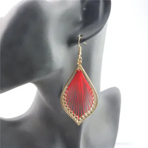 Primer plano detallado de pendientes colgantes metalicos huecos con hilo rojo bohemio.