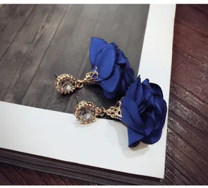 Close-up detail of royal blue fabric rose earrings with sparkling rhinestone stud design.