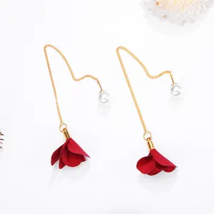 Close-up detail of the long gold-tone tassel earrings featuring red fabric flower petals and pearls.