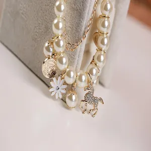 Detalle de pulsera de perlas multicapa con dije de poni de diamantes y flor delicada.