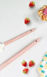 Gros plan détaillé de la spatule en silicone avec manche en bois, trou et motif de fruits.