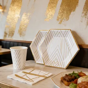 Set di piatti e bicchieri di carta esagonali a righe dorate per decorazione tavola principale.