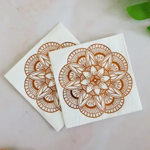 Disposable paper napkins with golden floral mandala pattern for party table decor.