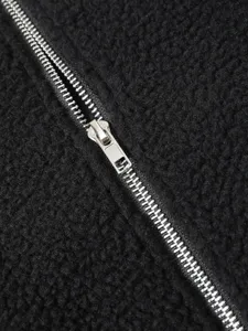 Detailed view of the metallic zipper on a cozy black sherpa fleece jacket texture.