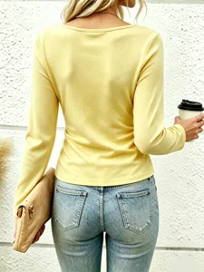 Back view detail of casual solid yellow long sleeve top paired with blue jeans and clutch.
