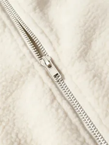 Close-up detail of cream sherpa fleece jacket with metal zipper, soft texture and warm winter style.
