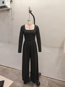 Black long sleeve square neck wide leg jumpsuit detail view in factory setting casual wear.