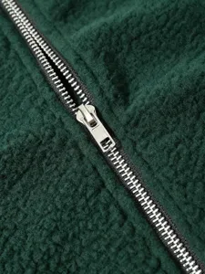 Close-up view of metal zipper and soft fluffy dark green fleece jacket fabric detail.