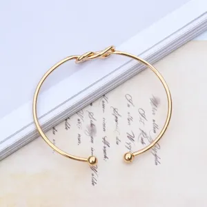 Elegant gold plated open cuff bracelet featuring a chic love knot design and smooth ball ends.
