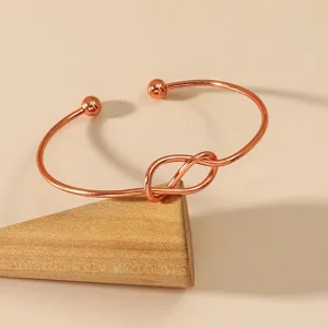 Minimalist rose gold tone open cuff bracelet with knot design, elegant adjustable wrist jewelry.