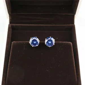 Detailed close-up shot of round blue cubic zirconia stud earrings displayed on brown velvet.