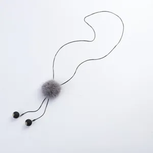 Long sweater chain necklace detail with a fluffy grey mink fur pom pom and dark pendants.