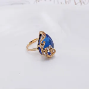 Close-up detail van een vergulde verstelbare ring met blauwe druppelkristal en steentjes.