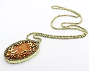 Primo piano dettagliato del ciondolo ambra ovale vintage con filigrana dorata e strass.