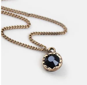 Vintage brass chain necklace detail featuring a dark faceted crystal stone pendant close up.