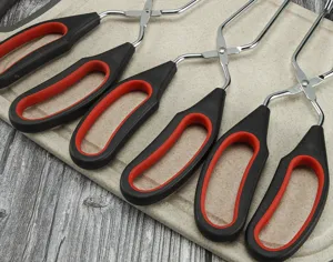 Stainless steel kitchen scissor tongs with red black ergonomic handles for BBQ, steak and food serving detail view.