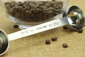 Stainless steel double-ended measuring spoon detail, featuring dual capacity scales for coffee.