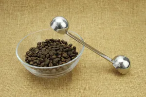 Stainless steel double ended coffee measuring spoon detail shot with beans bowl.